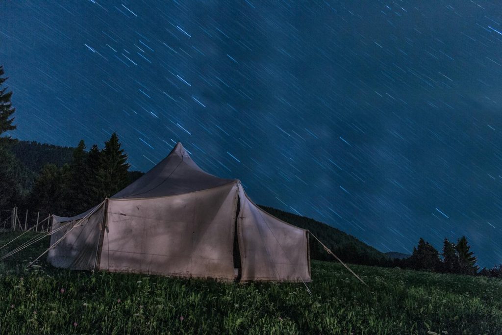 A serene night camping scene with a tent under star trails in the mountains.